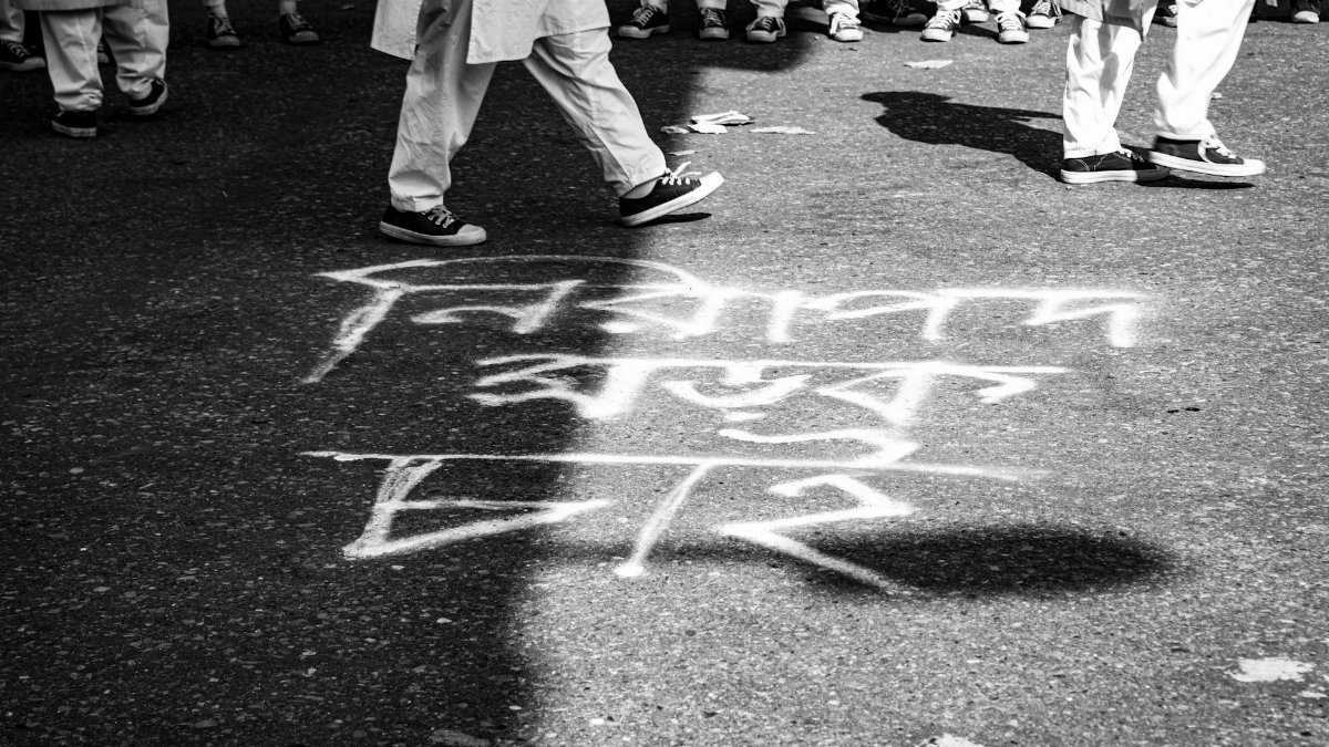 Monochrome photo capturing people walking over chalk writing on a city pavement.