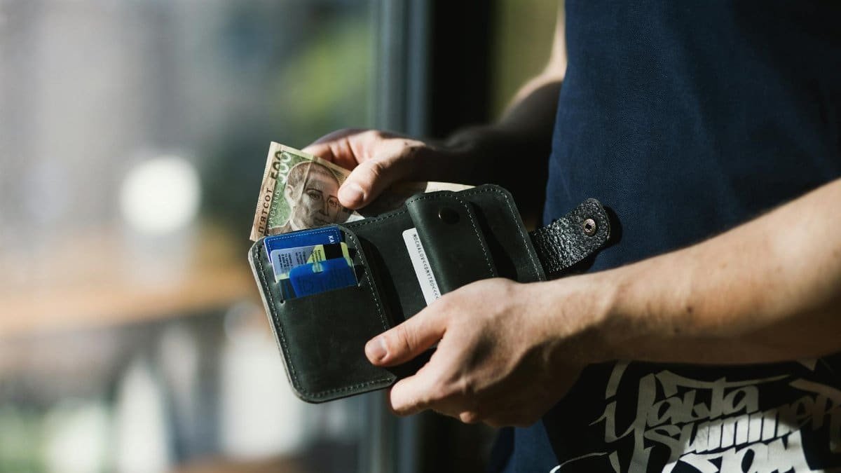 Close-up of a man holding a wallet with cash and credit cards, indoors.