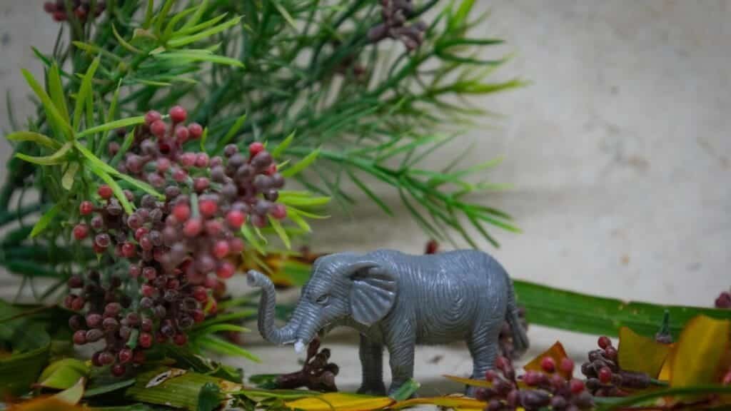 Toy elephant among lush greenery and berries for nature-inspired decor.