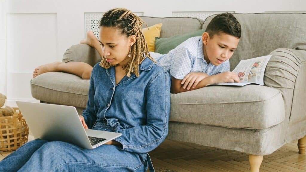 A mother and son enjoying leisure activities indoors with a laptop and book.