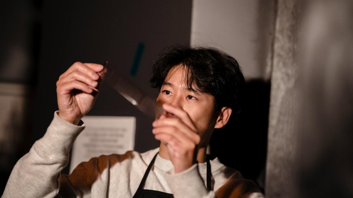 A man carefully inspects a film negative in a photography darkroom, focused on the developing process.