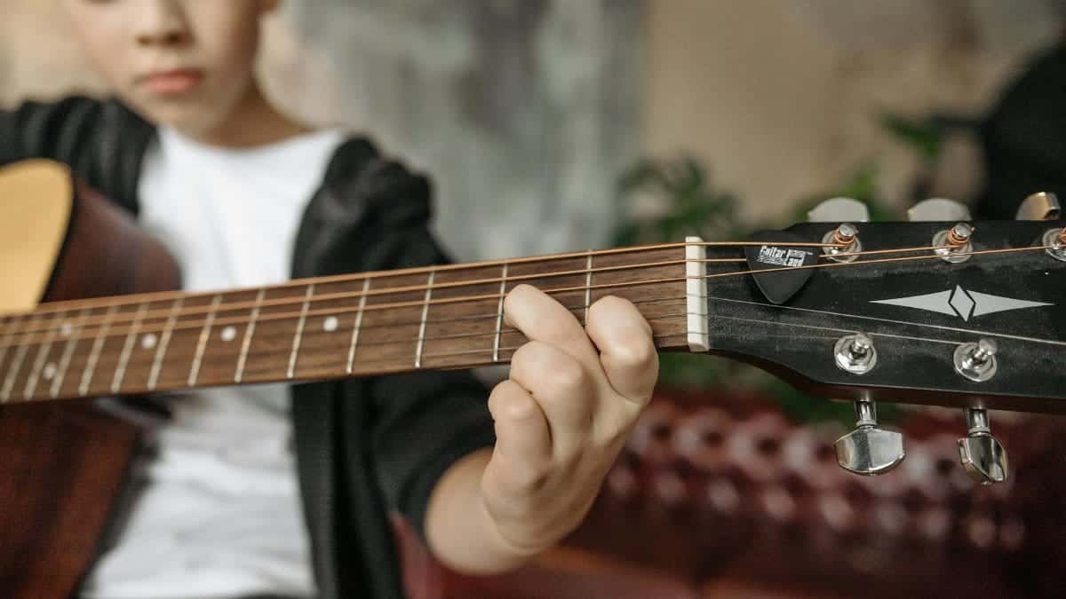 A child playing an acoustic guitar indoors with focus on fretboard and fingers.