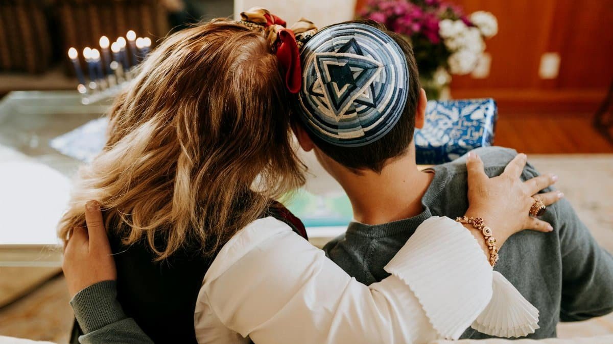 A warm embrace between family members celebrating Hanukkah indoors with menorah lights.