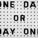 Black letters on white board saying 'One Day or Day One?' with polka dot design.