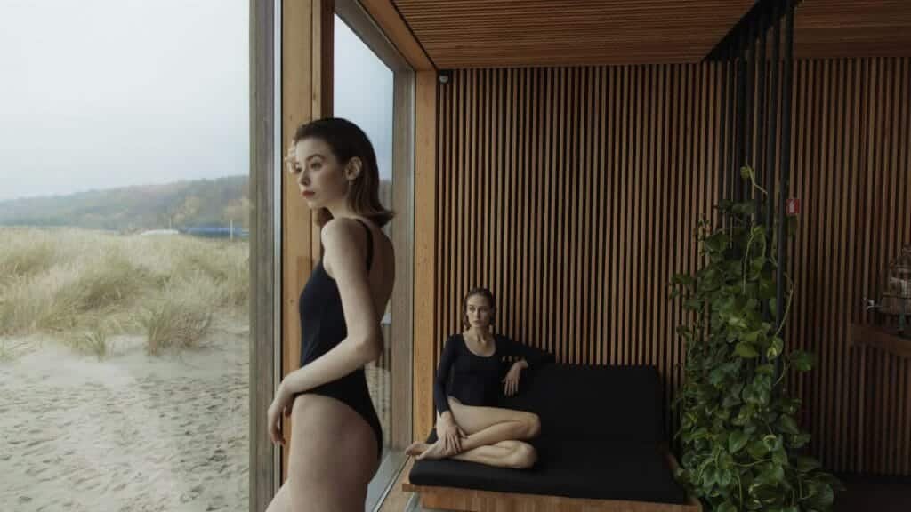 Two women in swimsuits relaxing indoors with a beach view, blending modern architecture with nature.