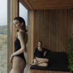 Two women in swimsuits relaxing indoors with a beach view, blending modern architecture with nature.