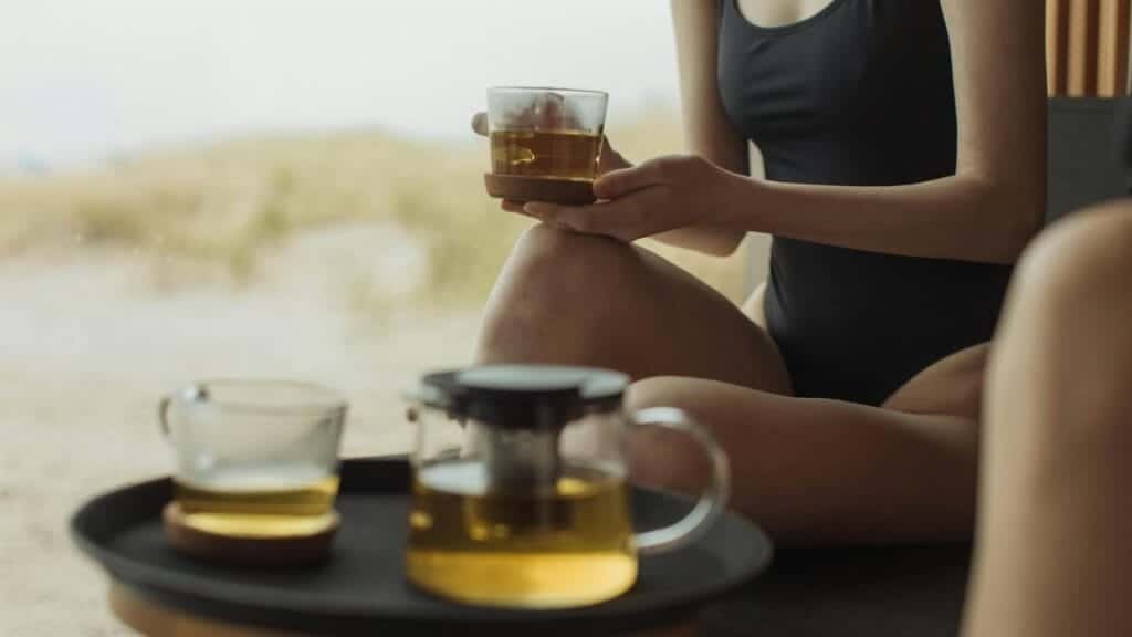 Two adults enjoying tea in swimwear indoors with a seaside view, embracing relaxation.