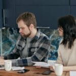 A couple reviews bills and finances at a desk with a laptop and papers. Indoor setting, focused on budgeting.
