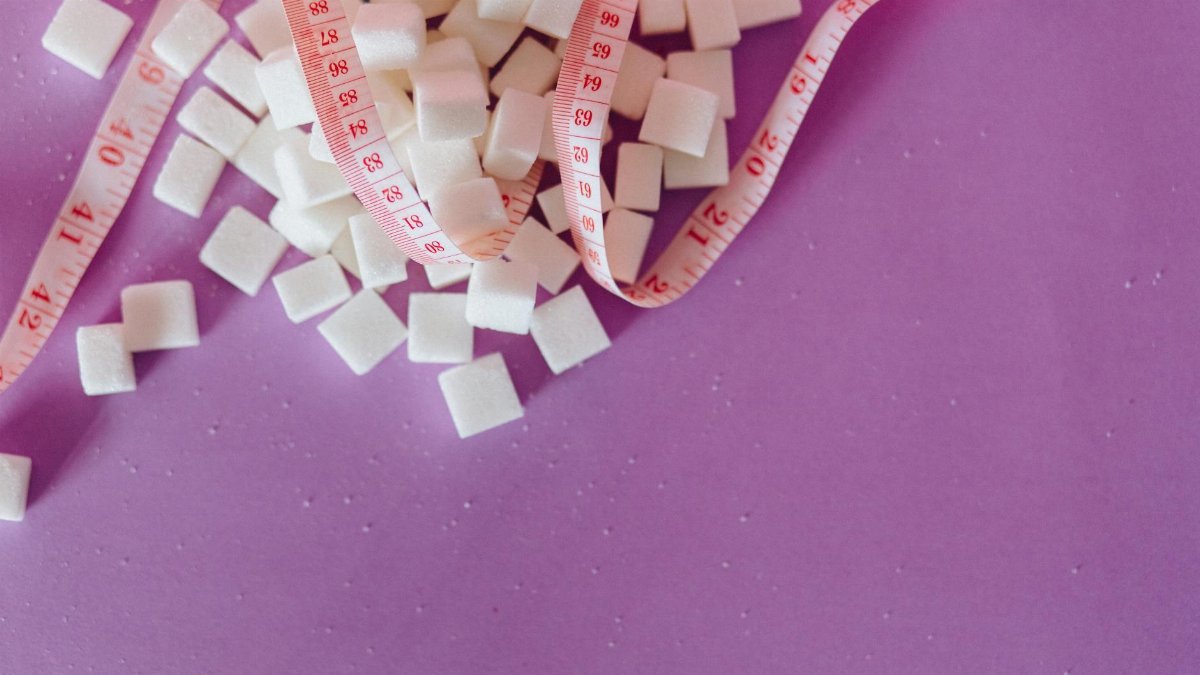 White sugar cubes with a pink tape measure on a purple surface, symbolizing diet awareness.