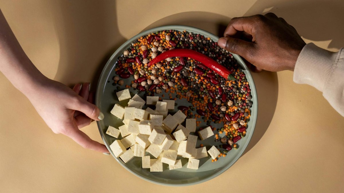 A diverse plate with tofu, legumes, and a chili pepper. Hands shown.