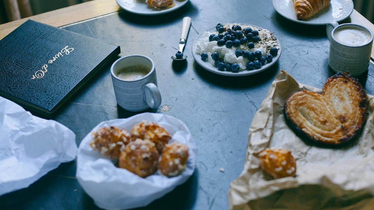 A charming breakfast scene featuring pastries, coffee, and a blueberry yogurt parfait on a table.