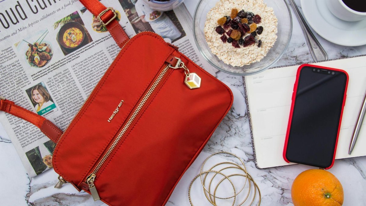 Flat lay showcasing a vibrant orange bag, oatmeal breakfast, coffee, phone, and newspaper for a stylish morning.