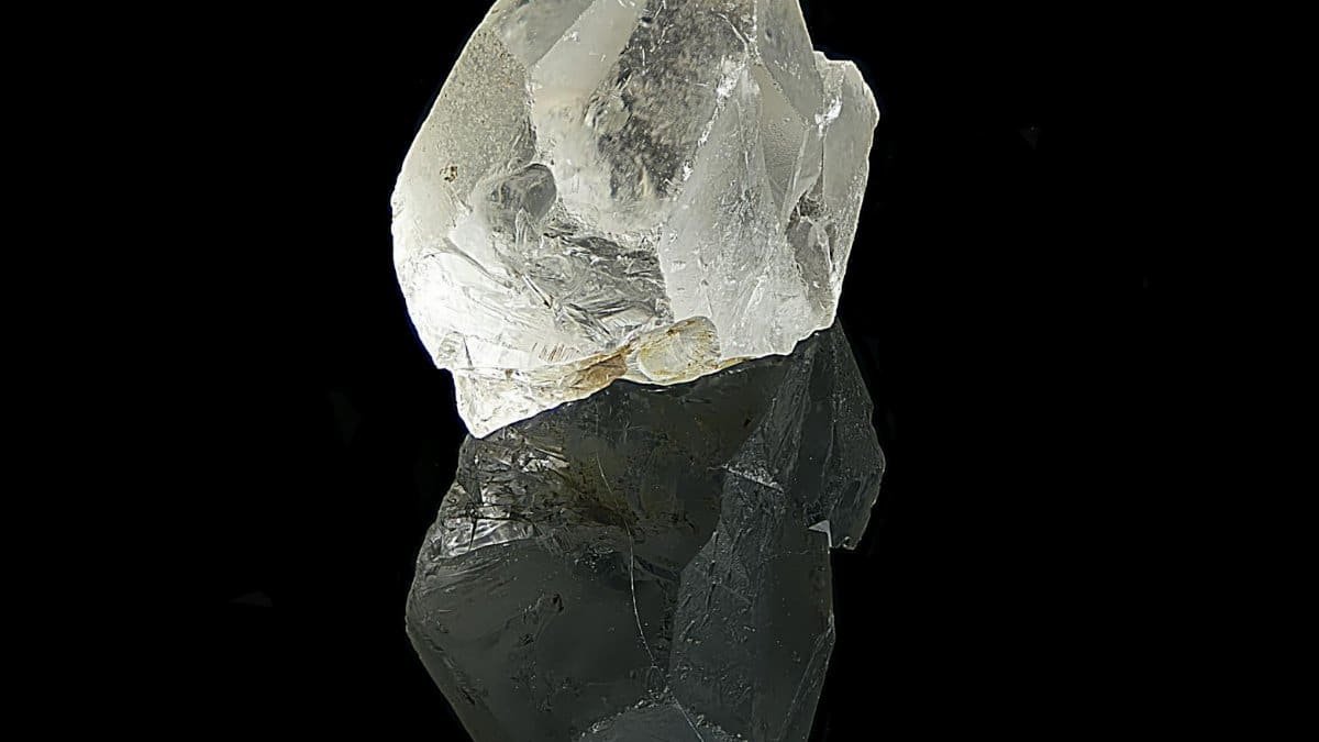 Clear quartz crystal with reflection against black background, showcasing natural beauty.