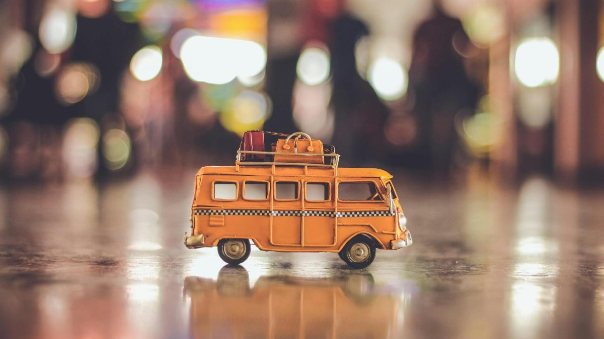 Close-up of a toy yellow campervan with luggage on a reflective surface and blurred lights.