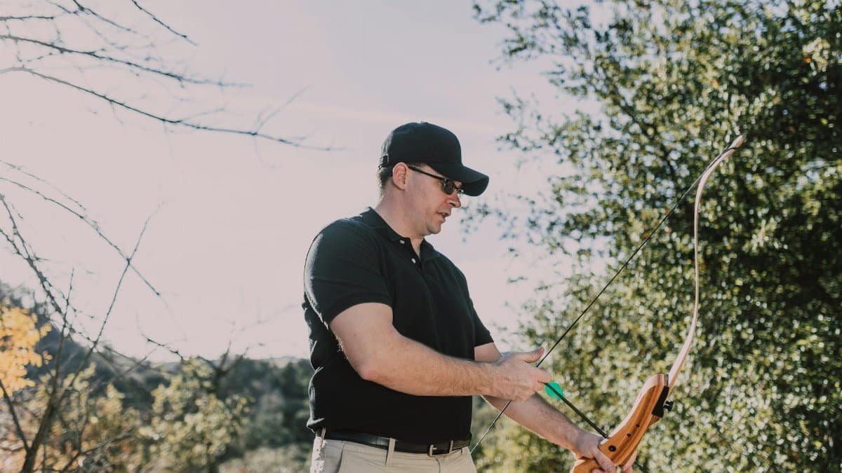 Man practicing archery outdoors with recurve bow, focusing on aim.