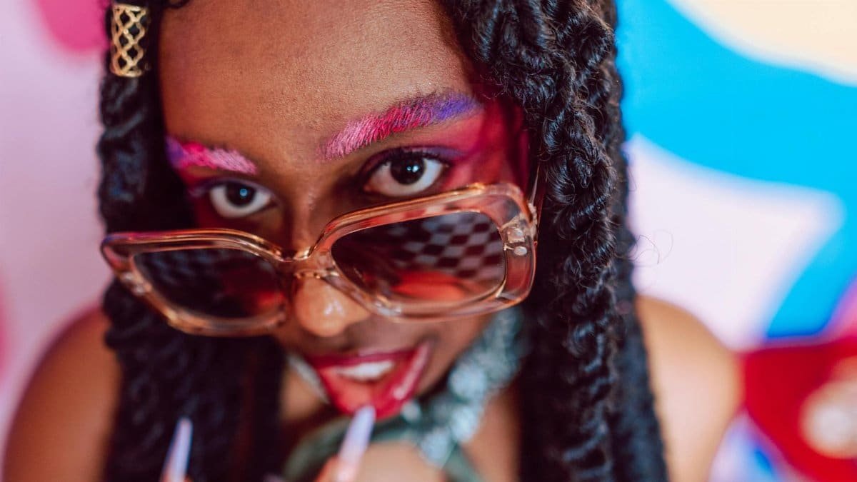 Vibrant portrait of a woman in sunglasses, featuring bold makeup and colorful eyebrows.