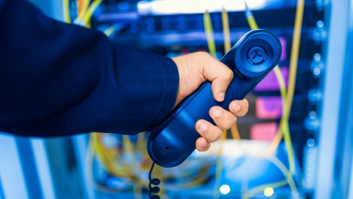 Close-up of a hand holding a telephone receiver in a server room emphasizing technology.