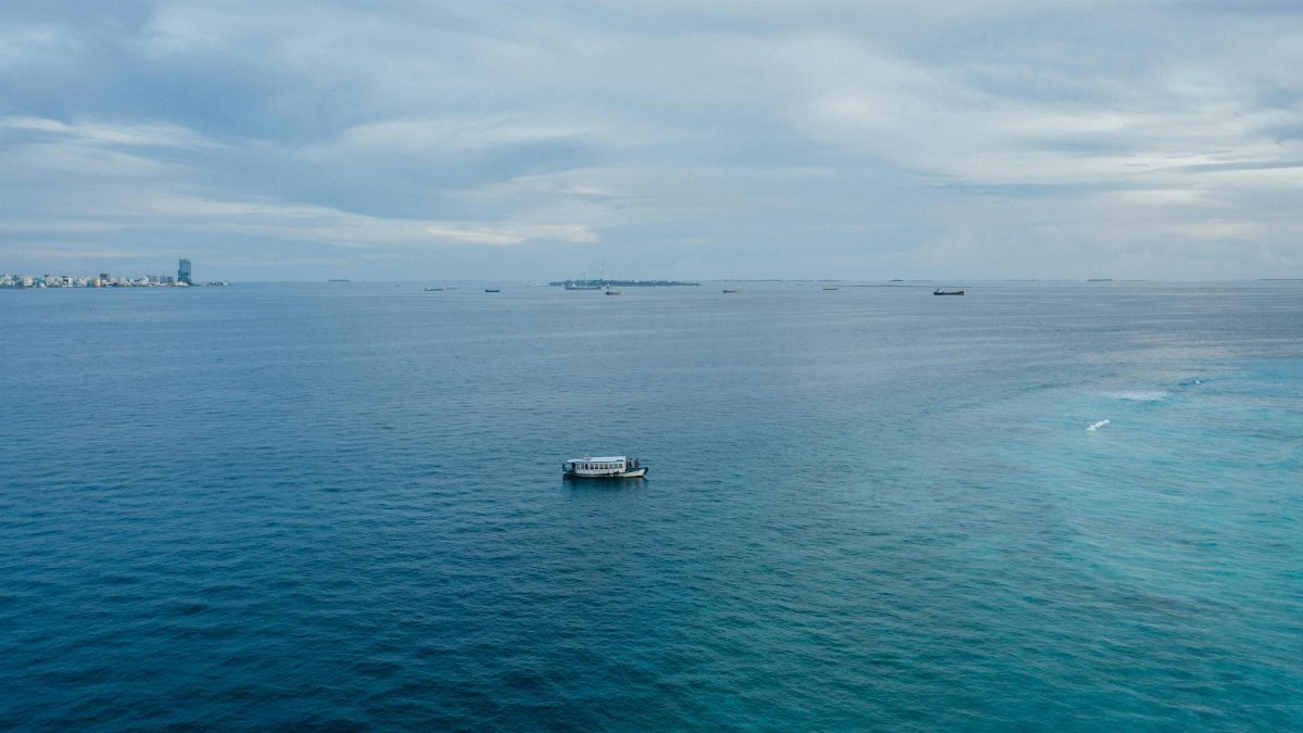 A tranquil ocean scene with a lone boat and a distant city skyline on the horizon.