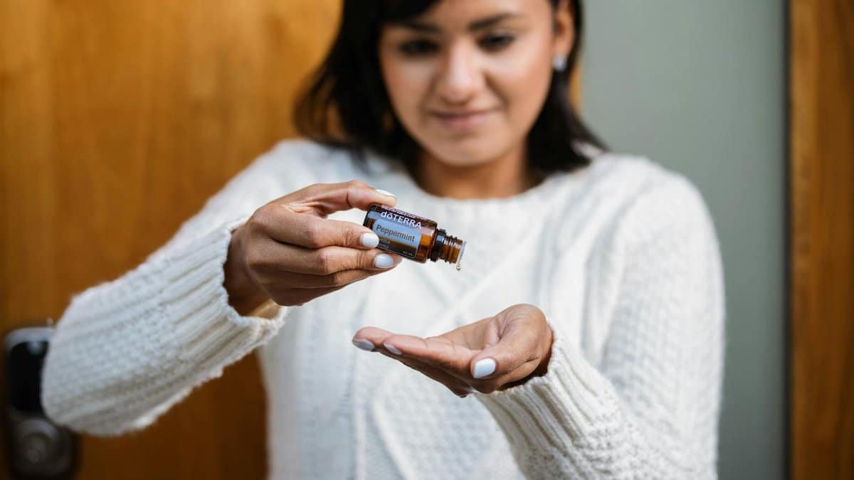 A woman pours peppermint essential oil into her hand indoors, focusing on aromatherapy.