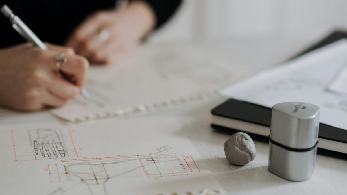 Detailed hand sketching on architectural blueprints with drawing tools and notebook.