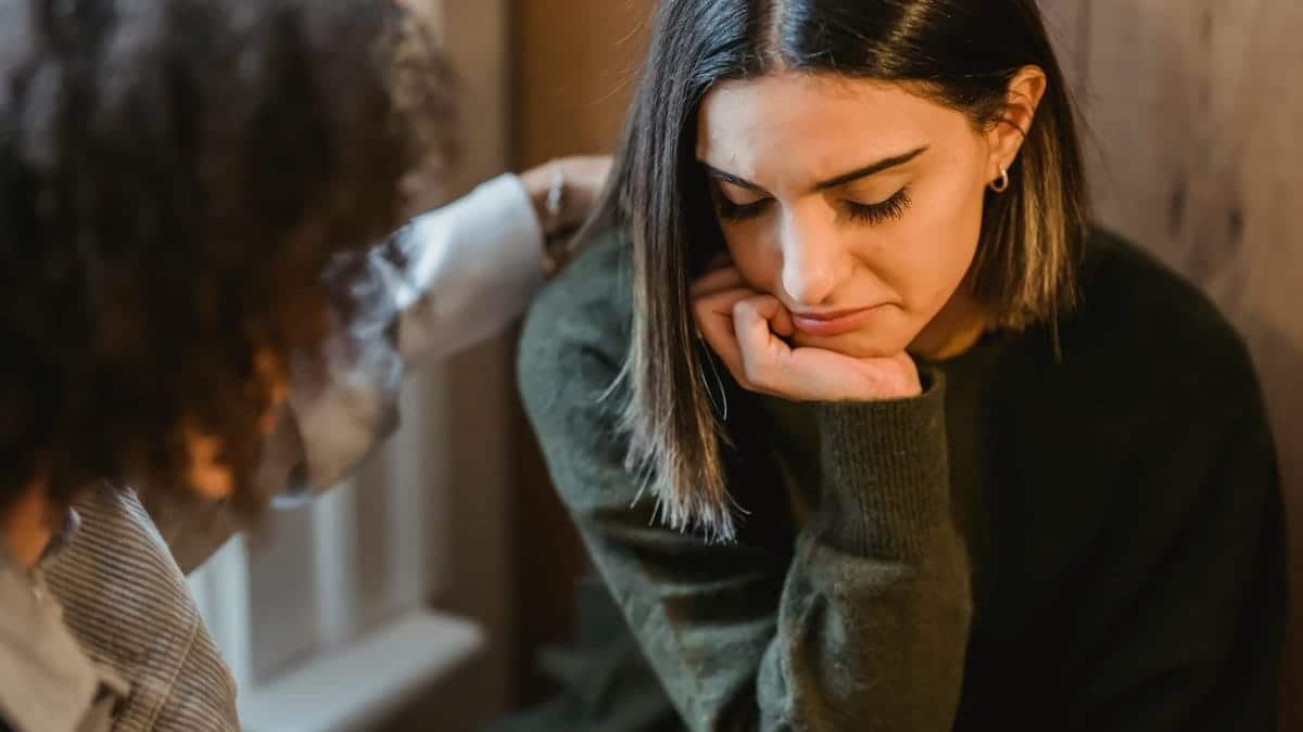 Crop woman tapping shoulder and comforting upset female friend while sitting at home together