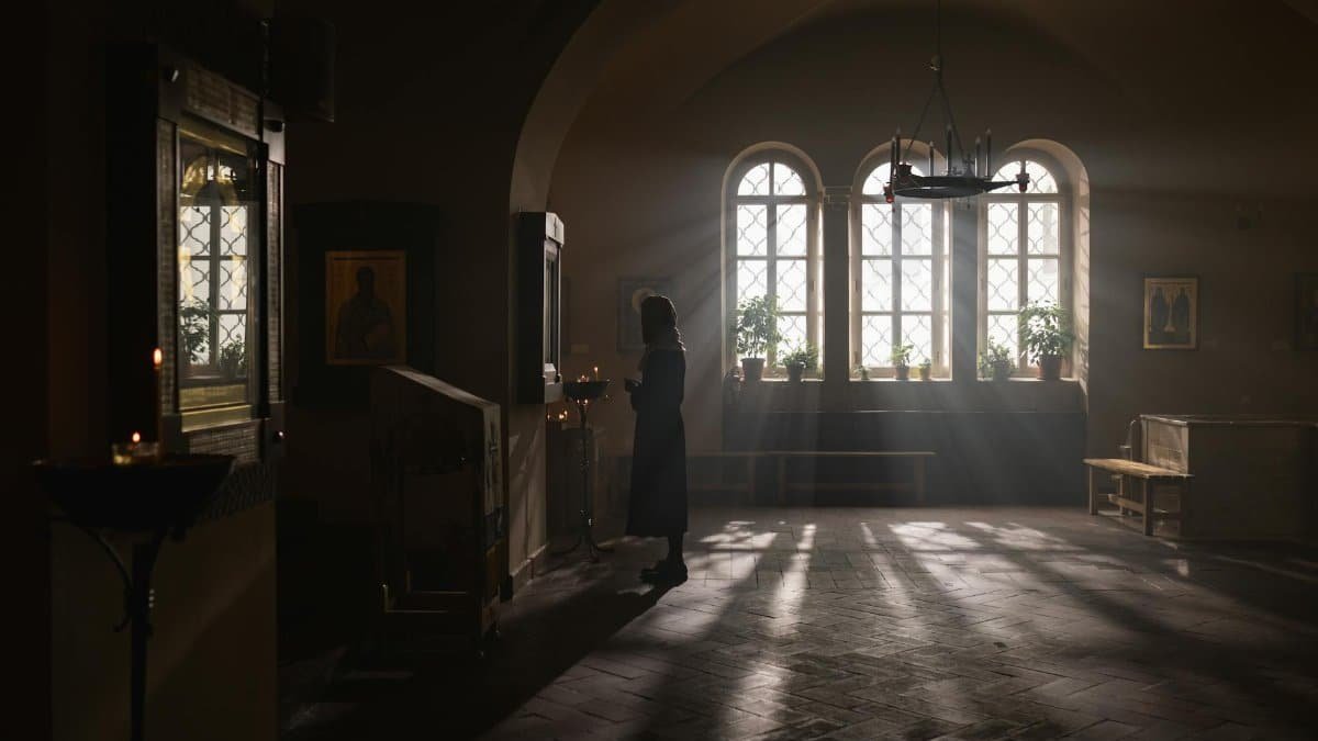 Silhouette of a woman standing in a serene, softly lit church interior with windows casting light.