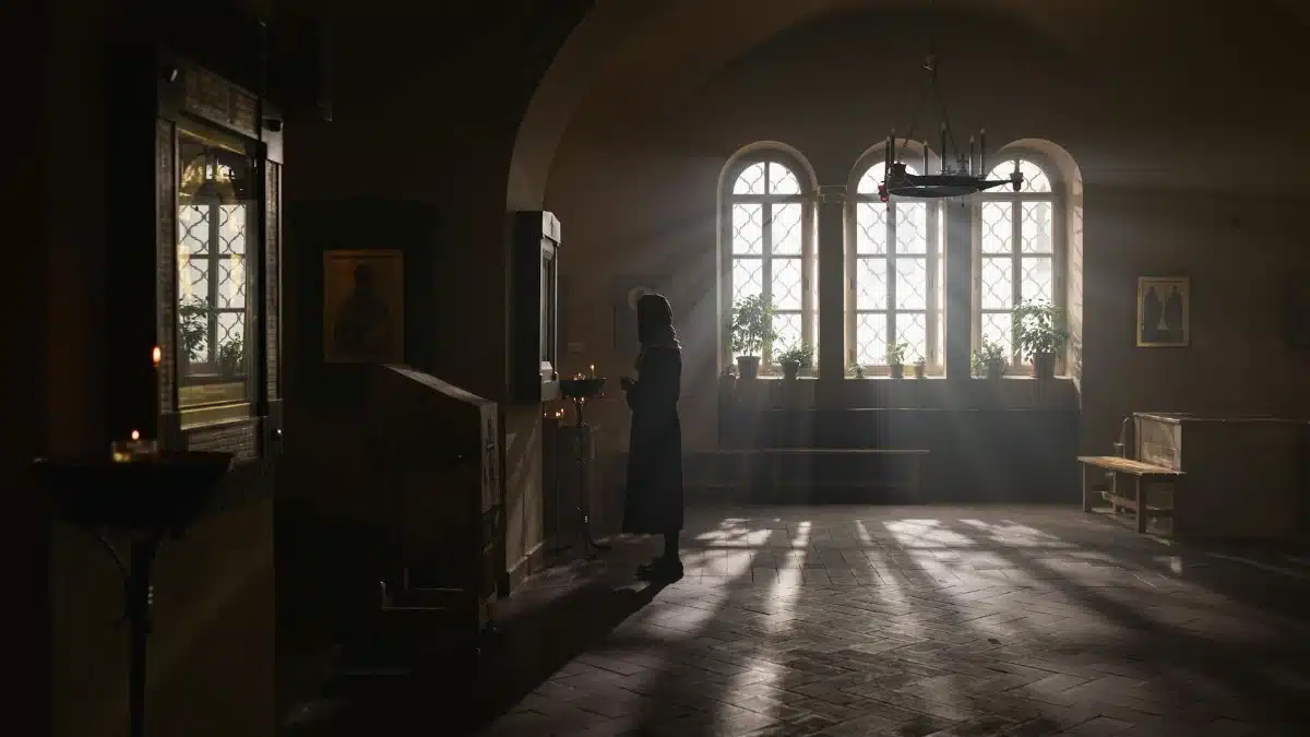 Silhouette of a woman standing in a serene, softly lit church interior with windows casting light.