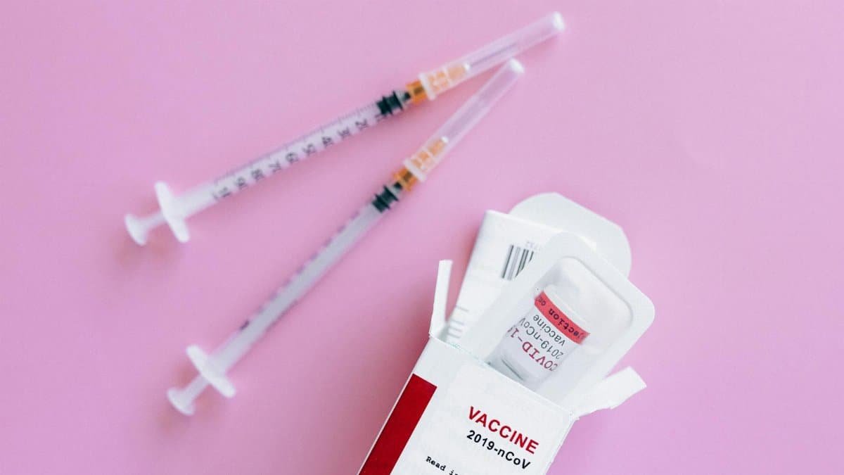 Close-up of vaccine vial and syringes on a pink background, representing healthcare.