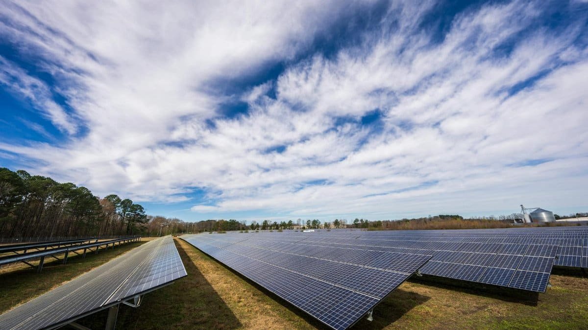 Solar panels spread across a field under a bright blue sky with clouds, showcasing renewable energy.