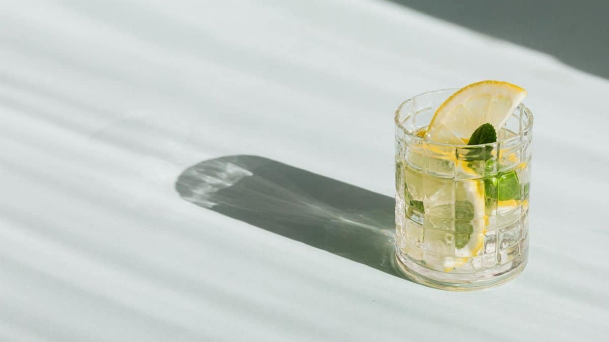 Flat lay of glass of fresh beverage with slices of lemon and leaves of mint placed on white background