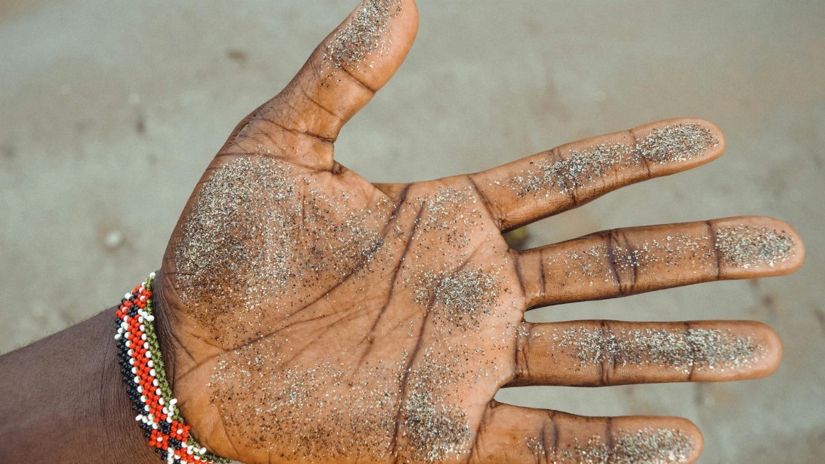 Close-up of an adult's sandy hand wearing a beaded bracelet on the beach.