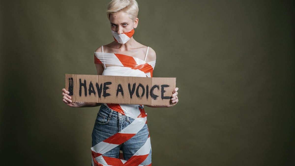A woman wrapped in tape holds a sign reading 'I have a voice,' symbolizing empowerment and freedom.