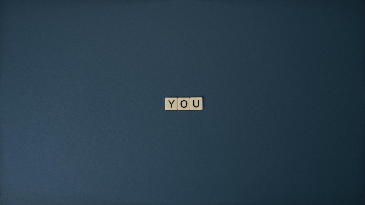 Flat lay of Scrabble letters spelling 'YOU' on a blue background, perfect for conceptual themes.
