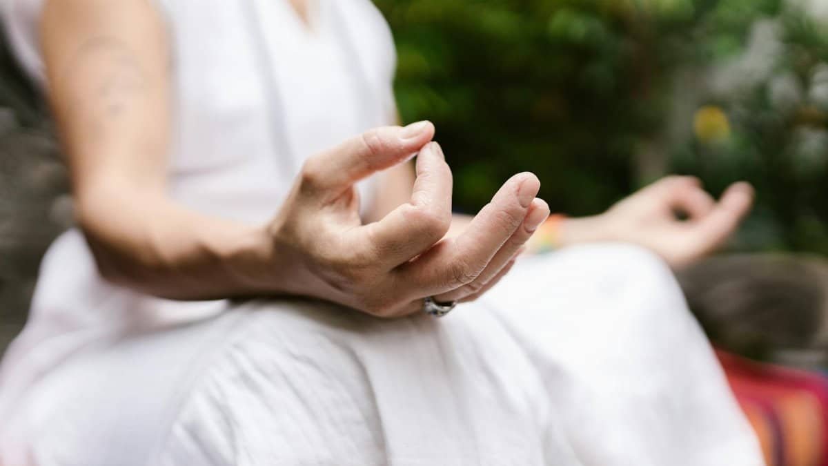 A person sits outdoors, focusing on their hands in a meditative mudra, embodying peace.