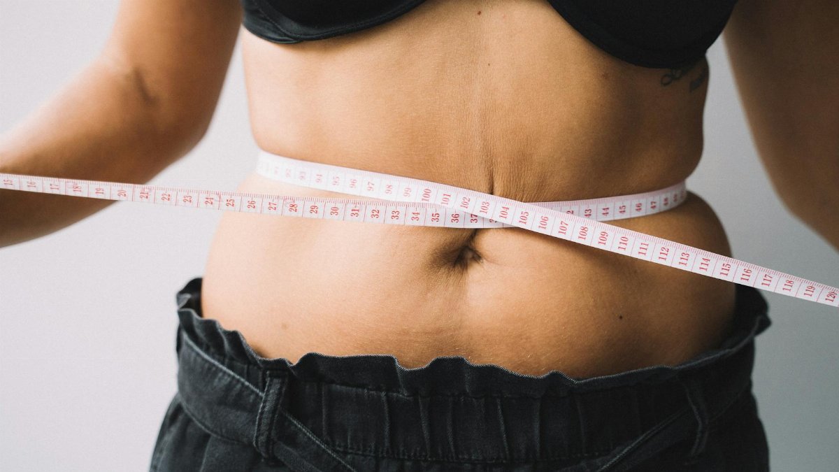 A person measuring their waist with a tape, symbolizing fitness and health goals.