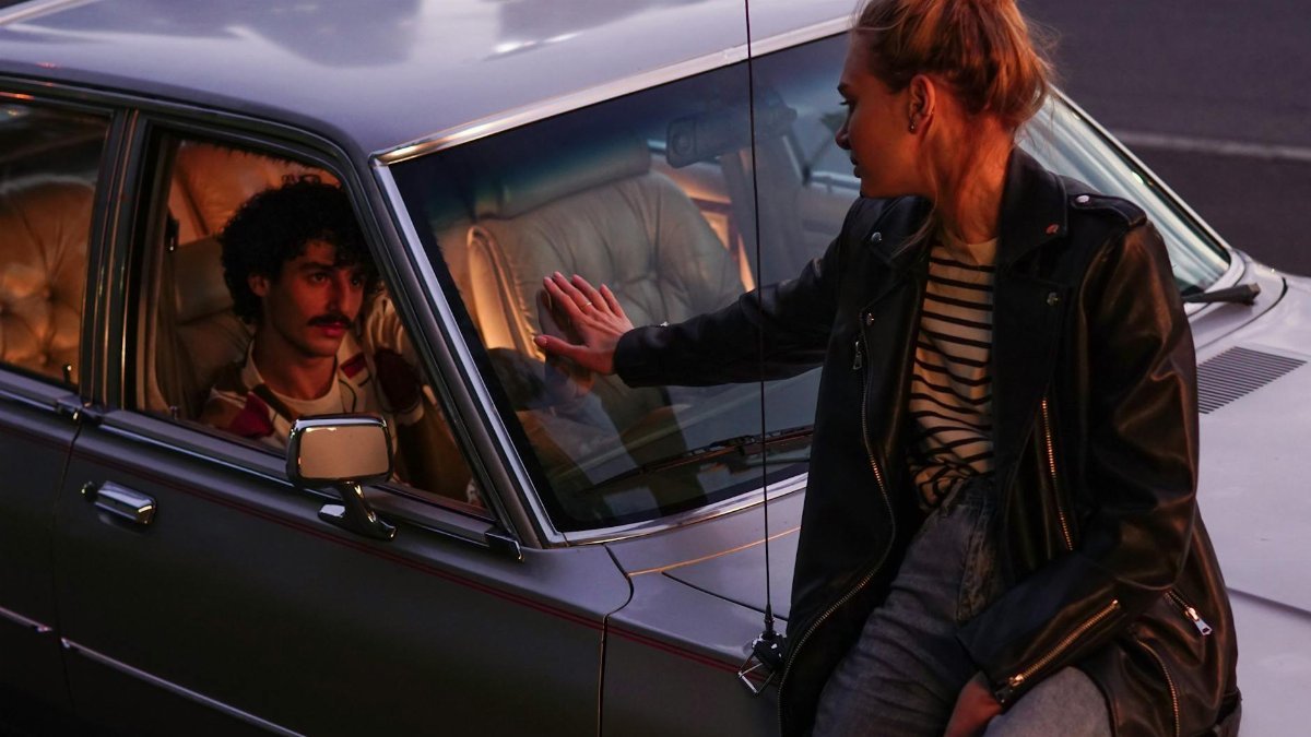 A dramatic moment between a couple by a classic car at dusk.