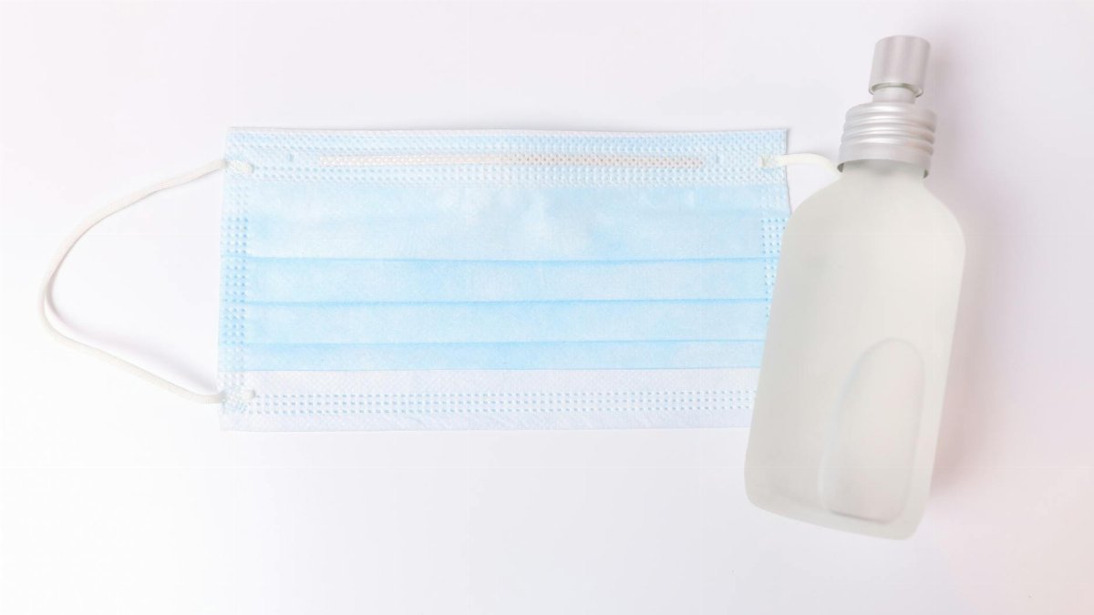 Blue surgical face mask and spray bottle on a white background, symbolizing cleanliness and health protection.