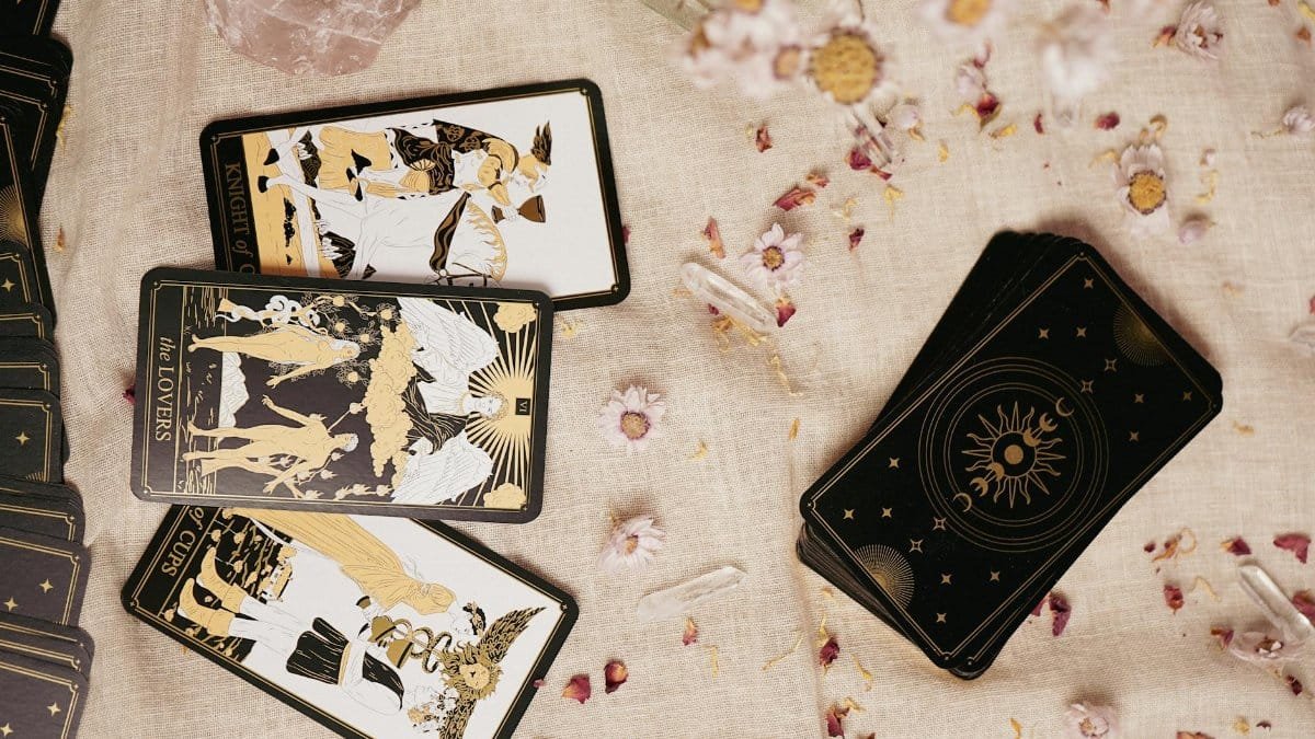 Flat lay of tarot cards on a fabric with flowers, crystals, and artistic details.