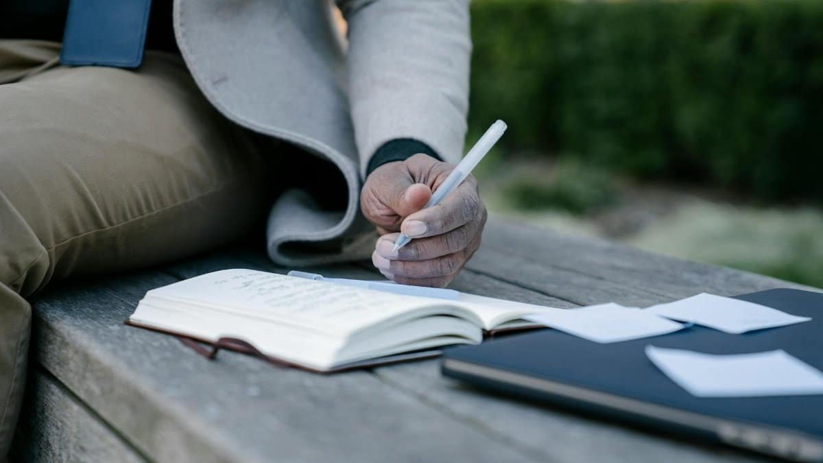 Close-up of a person writing in a notebook on a bench, conveying reflection and creativity outdoors.