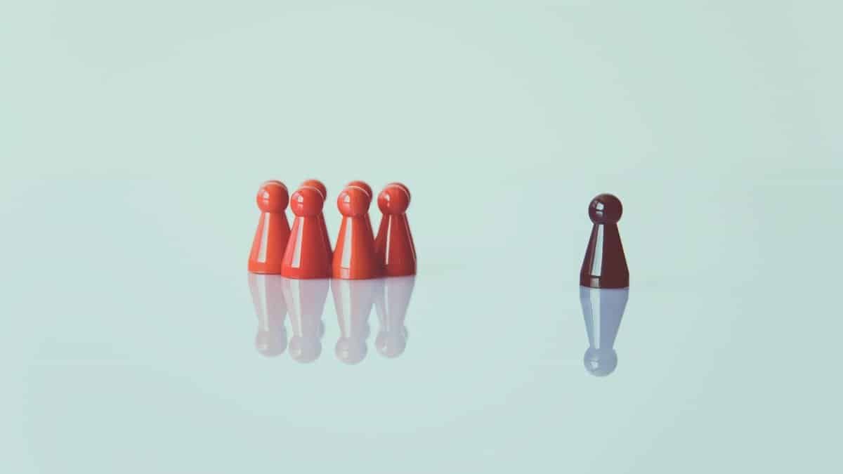 Red game pieces grouped with one isolated piece symbolizing social distancing on a reflective surface.