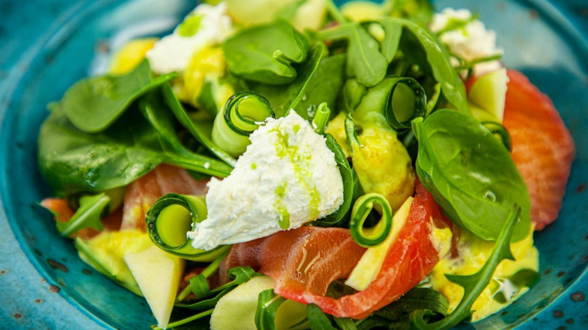 Delicious fresh salad with spinach, ricotta cheese, smoked salmon, cucumber, apple on a vibrant blue plate.