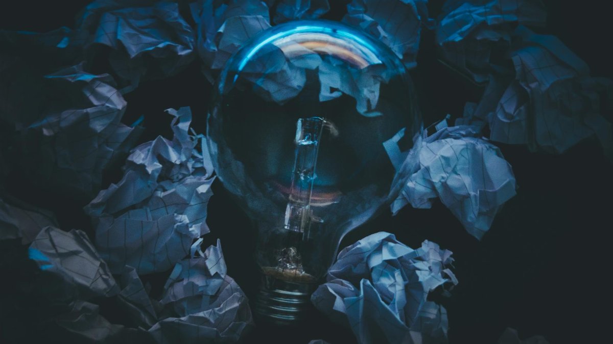 A light bulb surrounded by crumpled paper symbolizes creative ideas and innovation in a dark setting.