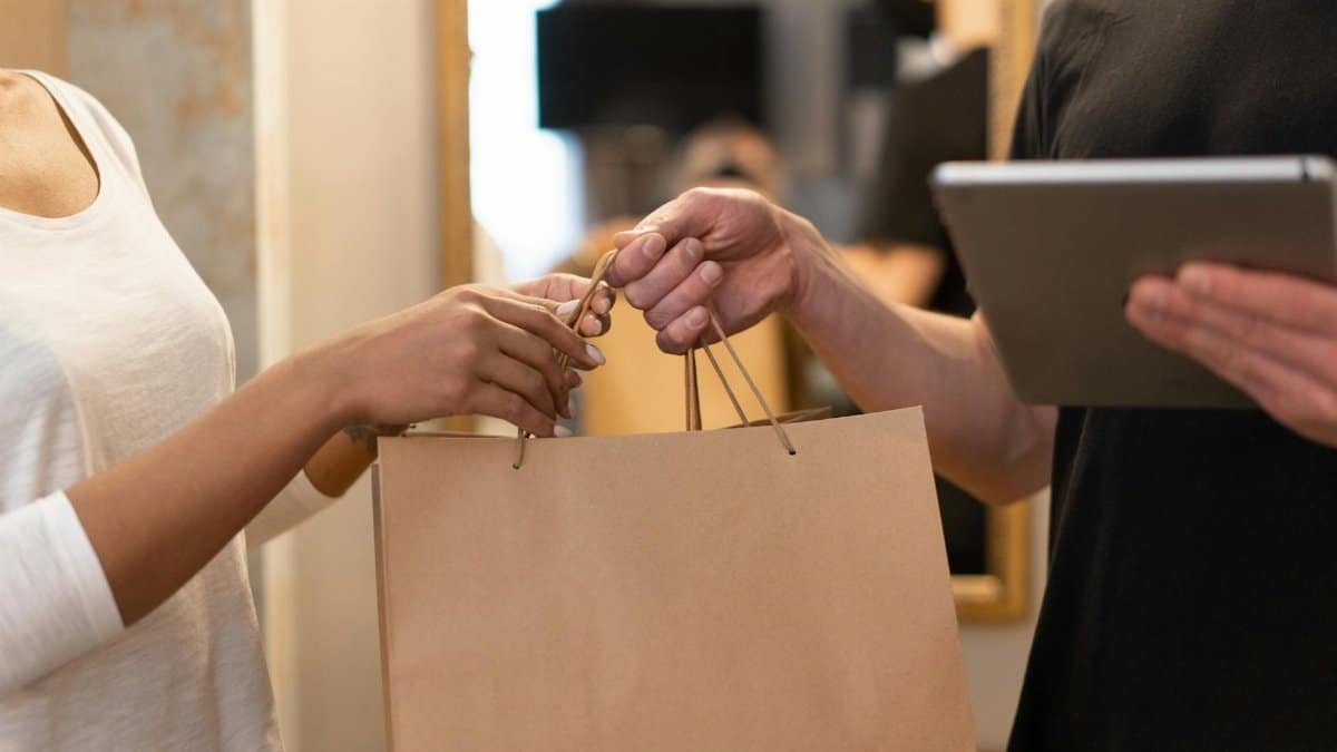 Close-up of hands exchanging a shopping bag indoors, symbolizing modern retail and technology.