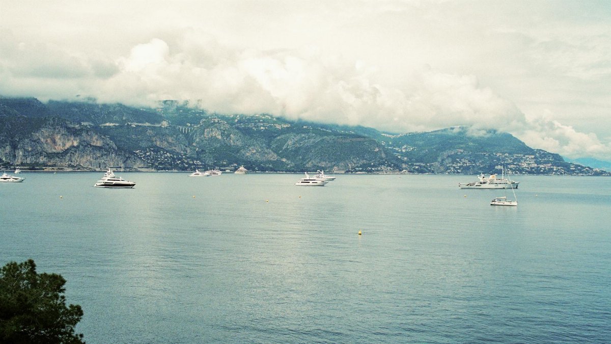 Scenic view of luxury yachts anchored along the stunning French Riviera coastline under a cloudy sky.