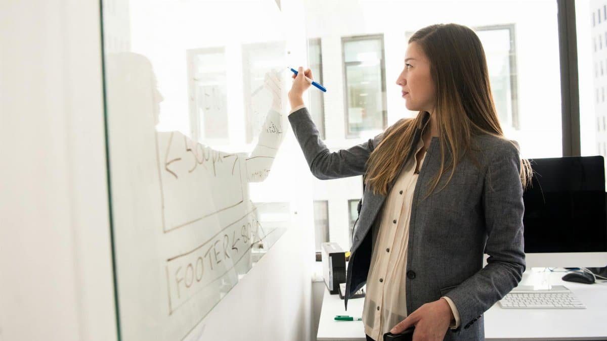 Professional woman writing on a whiteboard in an office environment, focusing on ideas.