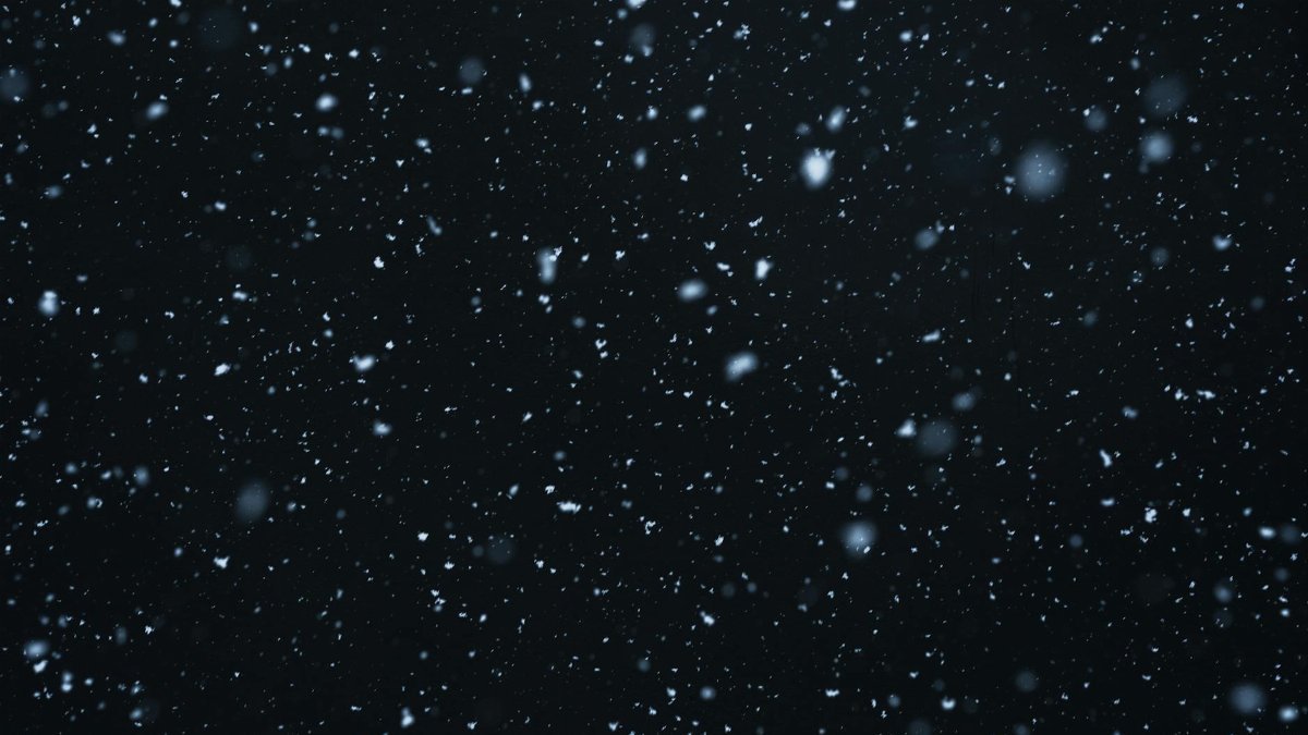 A mesmerizing view of snowflakes falling against a dark, starry night sky.