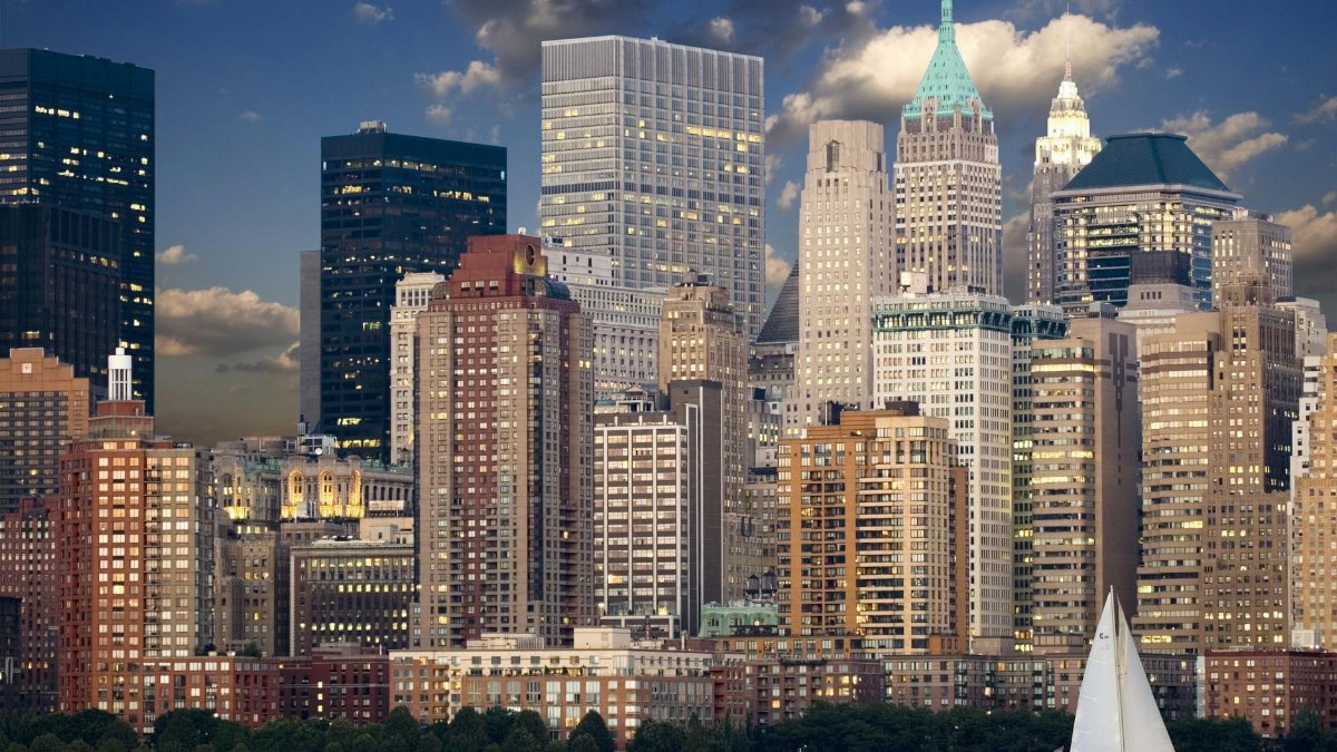 Panoramic view of New York City skyline with sailboat and river during twilight.