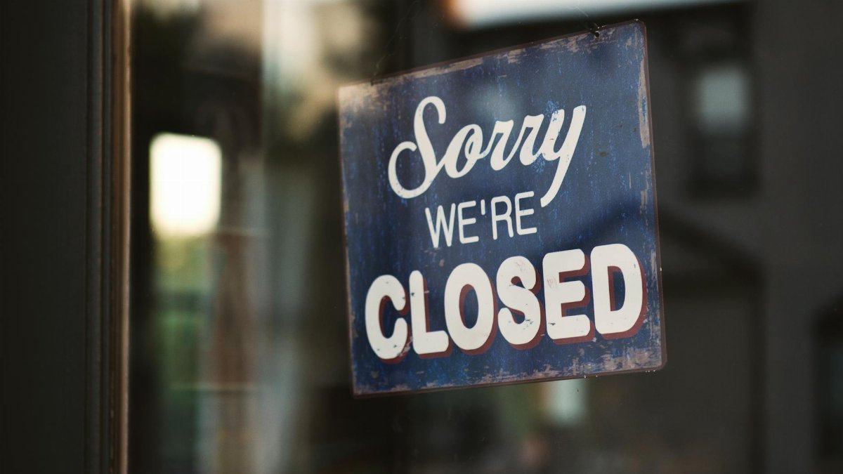A vintage "Sorry We're Closed" sign on a glass door reflects street view outside.