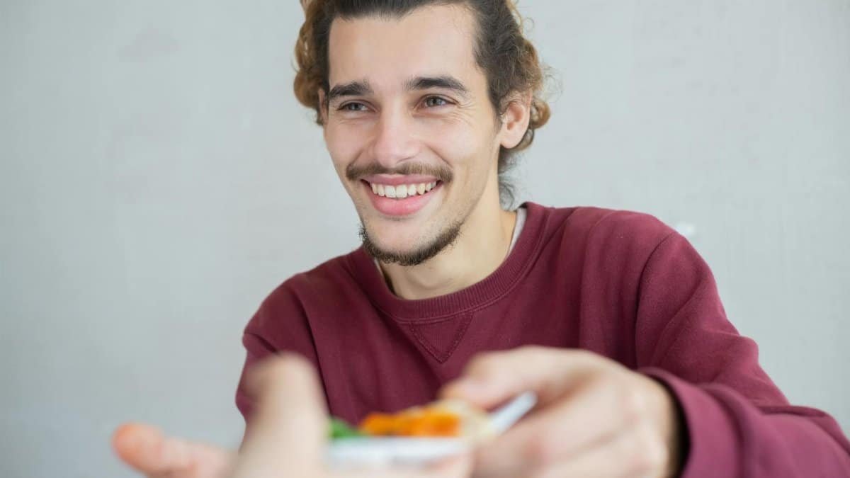 Smiling young man with beard and mustache sharing a meal indoors, expressing warmth and friendliness.