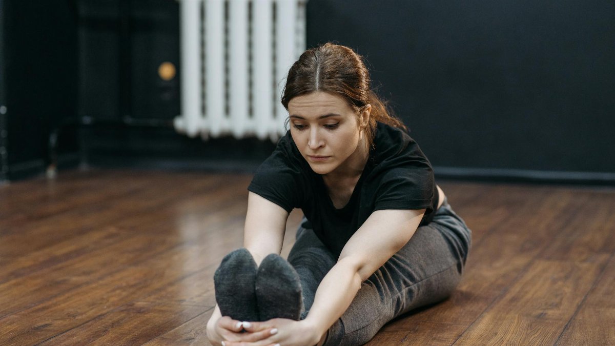 Adult woman performing seated stretch indoors, focusing on flexibility and fitness.